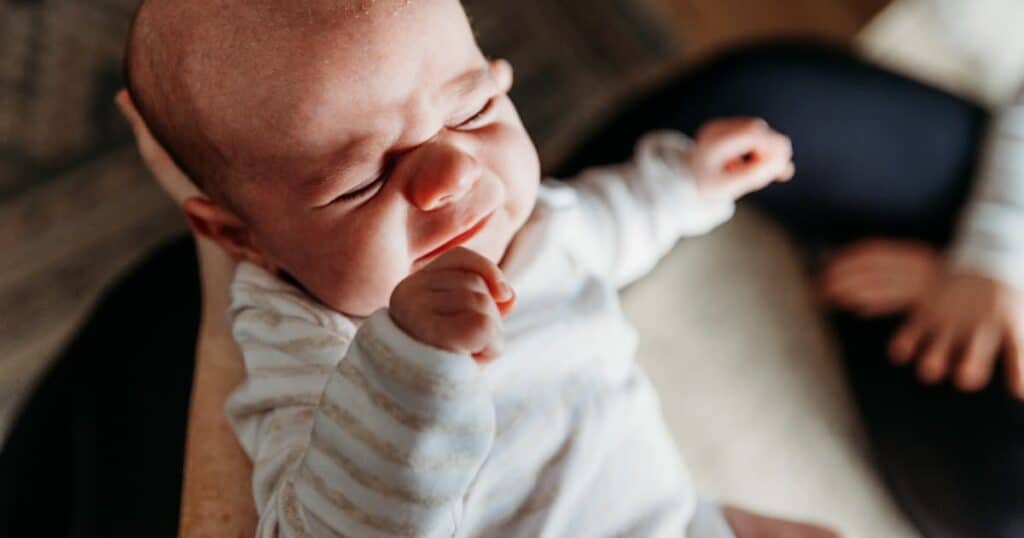Baby being held by Well Supported Family Newborn Care Specialist and squinting in the light.