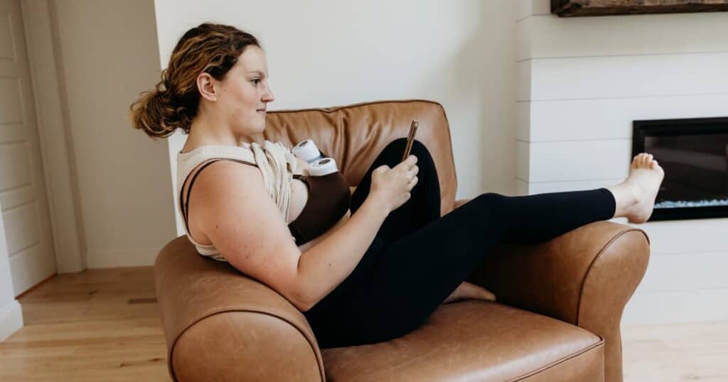 Mom reclining in leather chair using a wearable breast pump in her bra.