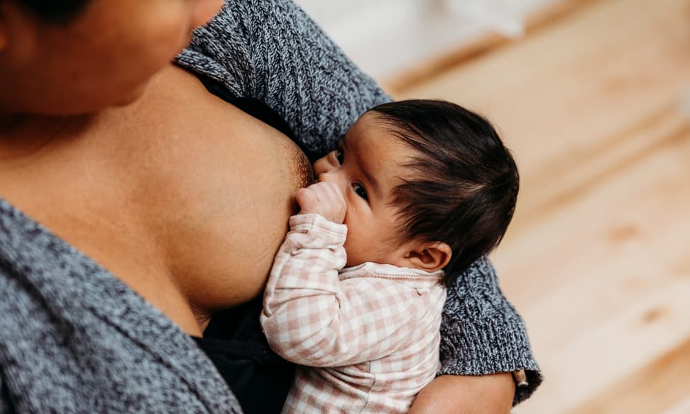 baby with dark hair breastfeeding while looking up at parent