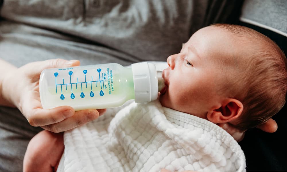 newborn baby drinking milk from a bottle with ounce markings