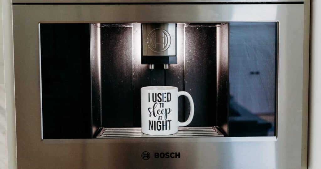 white coffee mug reading "I used to sleep at night" in black lettering, sitting in a coffee maker