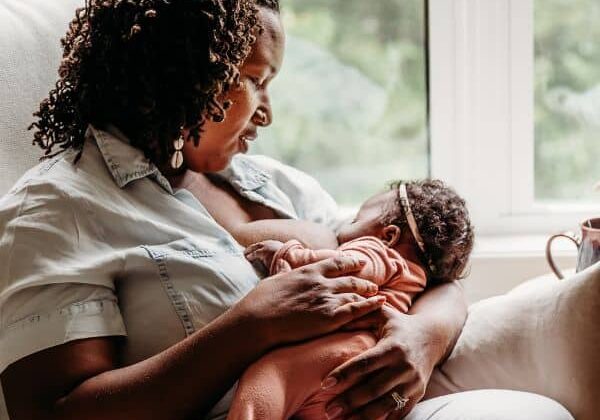 New mom breastfeeding baby in an armchair by the window