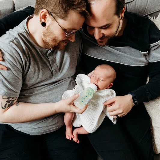 new dads bottle feeding newborn baby on couch