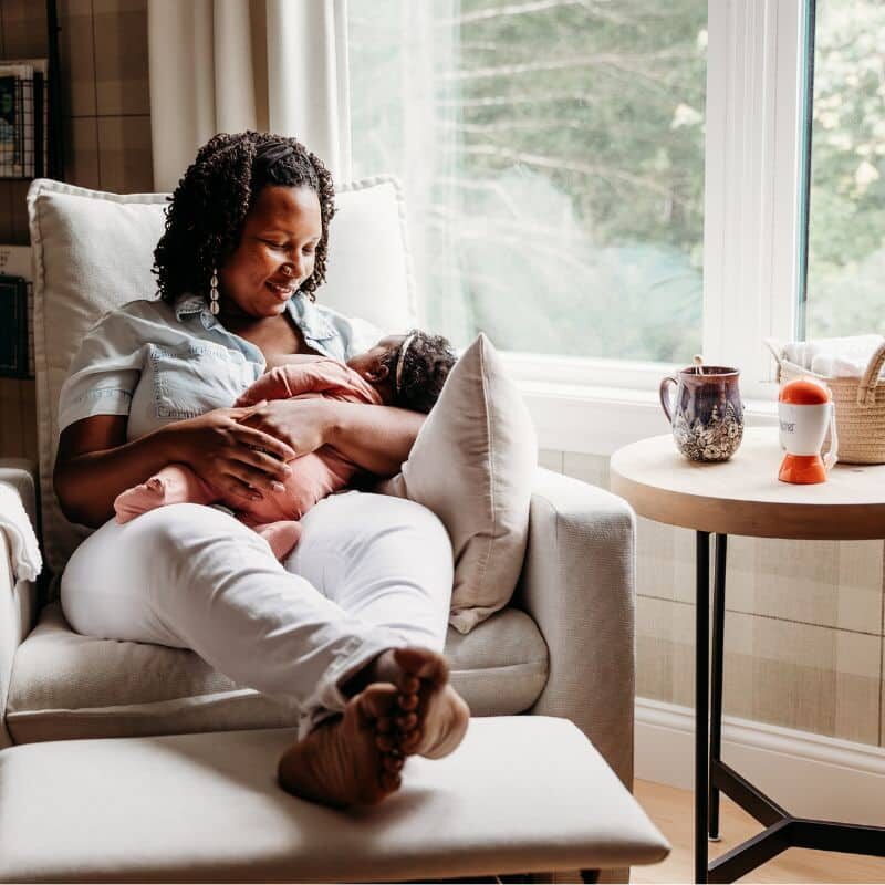 new mom bonding with her baby in armchair by window during daytime