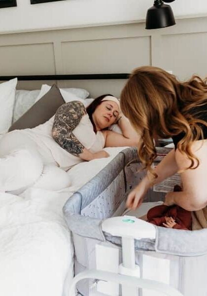 New mom resting in bed with doula by her side placing baby in the crib
